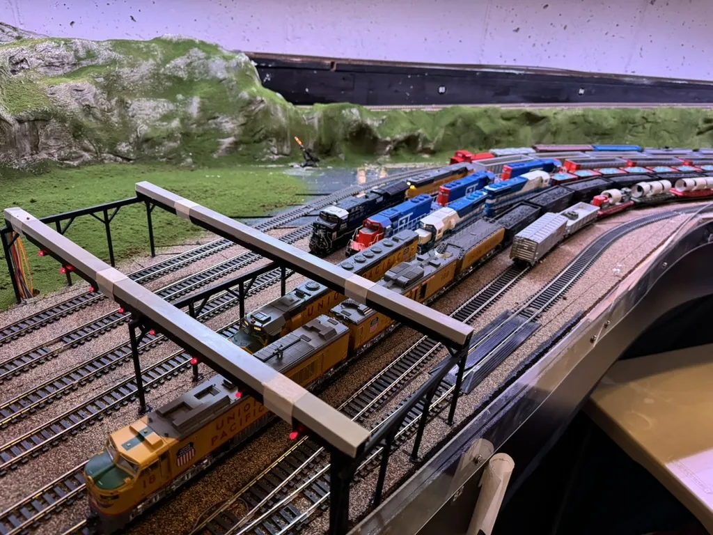 Model locomotives lined up beneath signal bridges on a detailed railroad layout